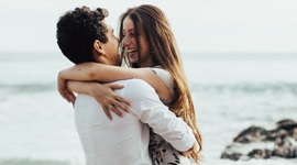 A photo of a man carrying a woman in his arms along the shoreline at a beach