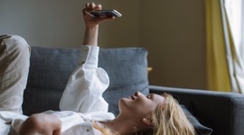 A photo of a woman lying on a couch, video calling with someone on the phone