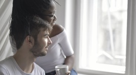 A photo of an interracial couple wearing white shirts, sitting down next to each other while looking out a window